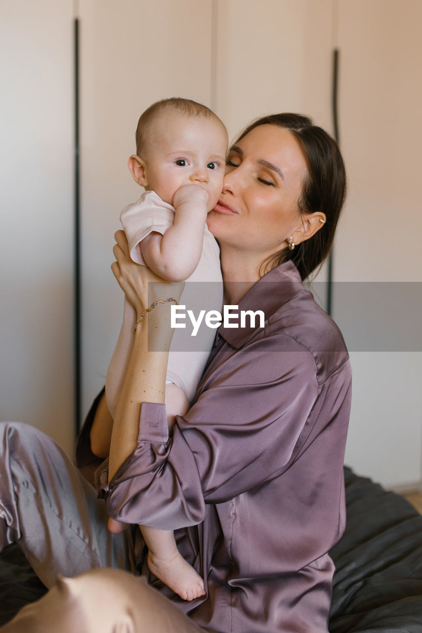 Mother lifts the baby up in her arms, kissing him on the cheek