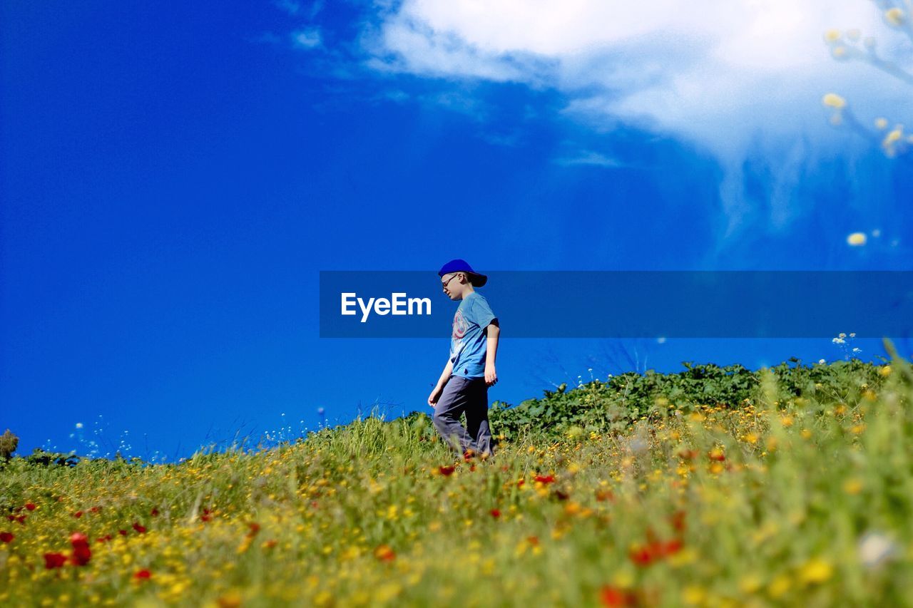 Low angle view of boy walking on grassy hill against sky during sunny day