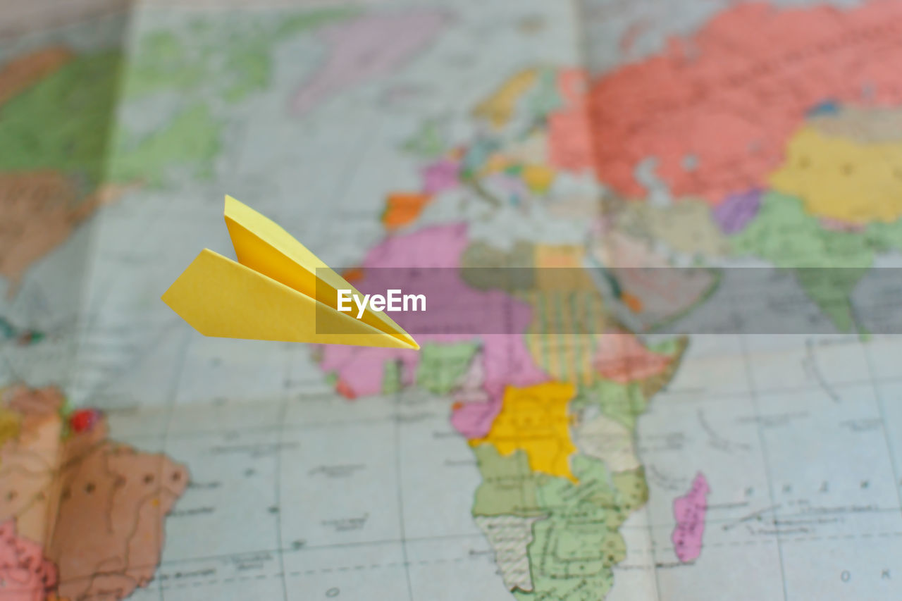 Close-up of yellow paper airplane flying over world map