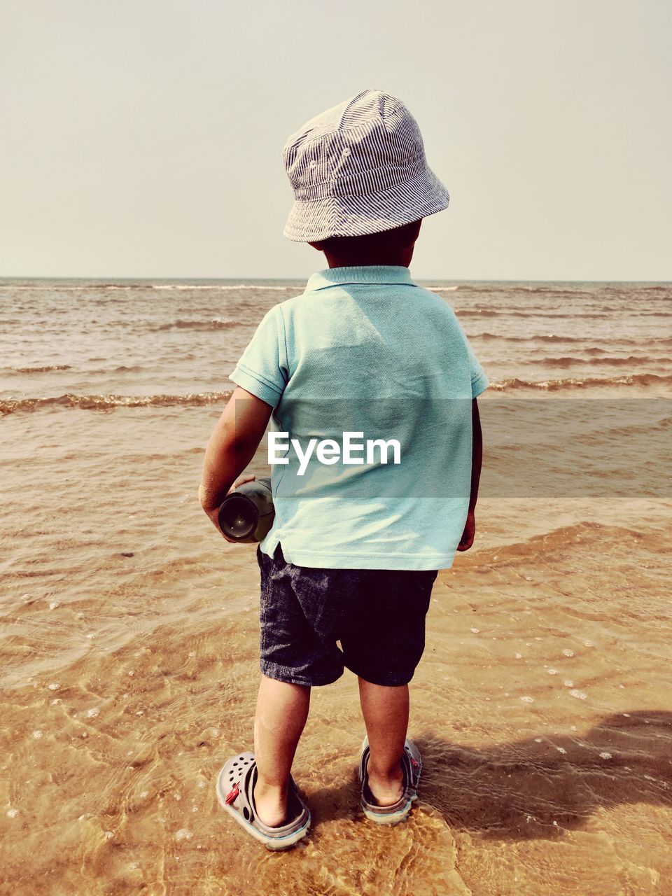 Rear view of boy standing at beach against clear sky