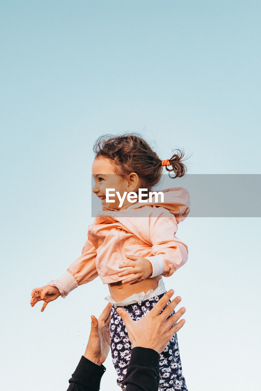 Cropped hands of person catching baby girl against clear sky