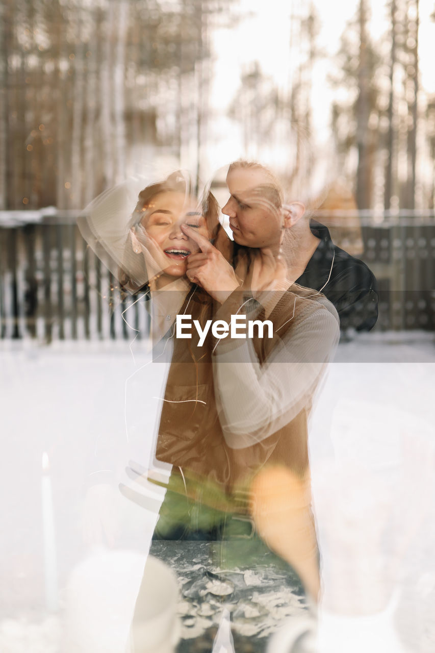 Portrait of a man and a woman in love hugging and kissing taken through the window of the house