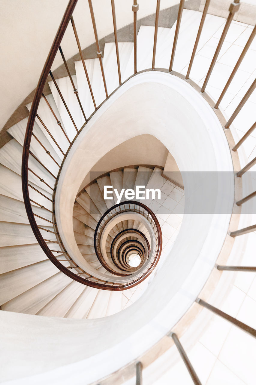 From above of white spiral stairs with wooden banister in bright contemporary building