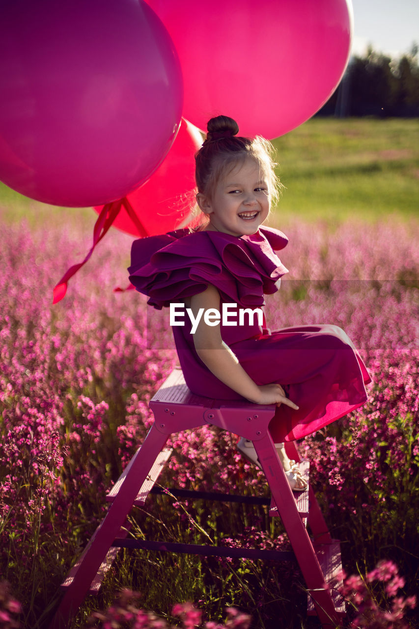  girl child of 5 years old is sitting on a pink stepladder,  dress in a field with pink flowers