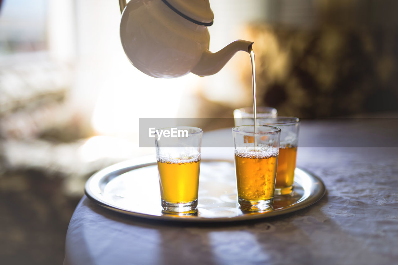 Pot pouring tea in glass on table