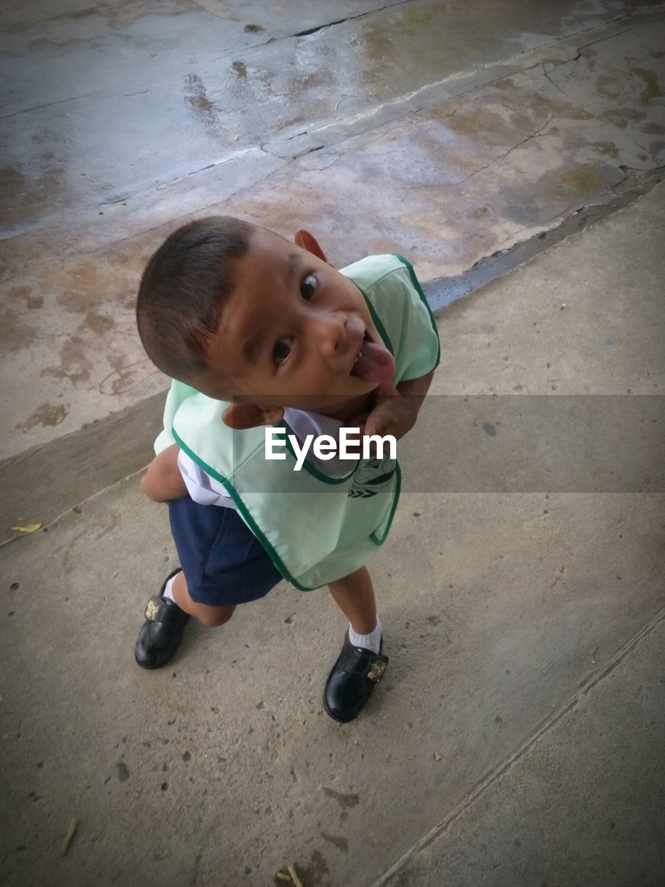 Portrait of cute schoolboy making face on wet footpath