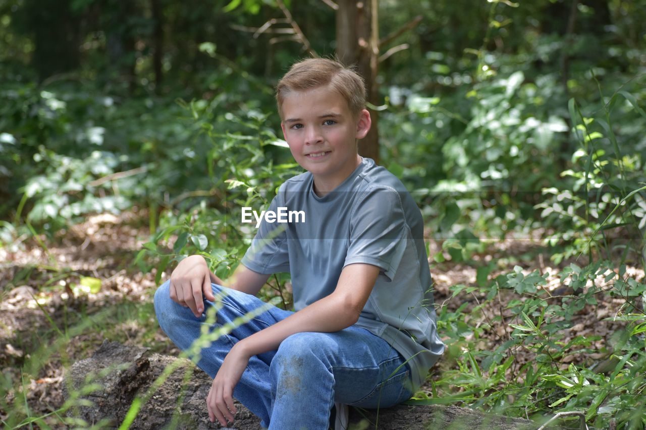 Portrait of smiling boy sitting on land in forest