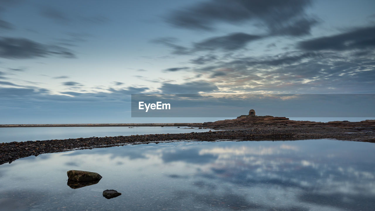 Old building on the coast at blue hour with clouds reflected in a rock pool