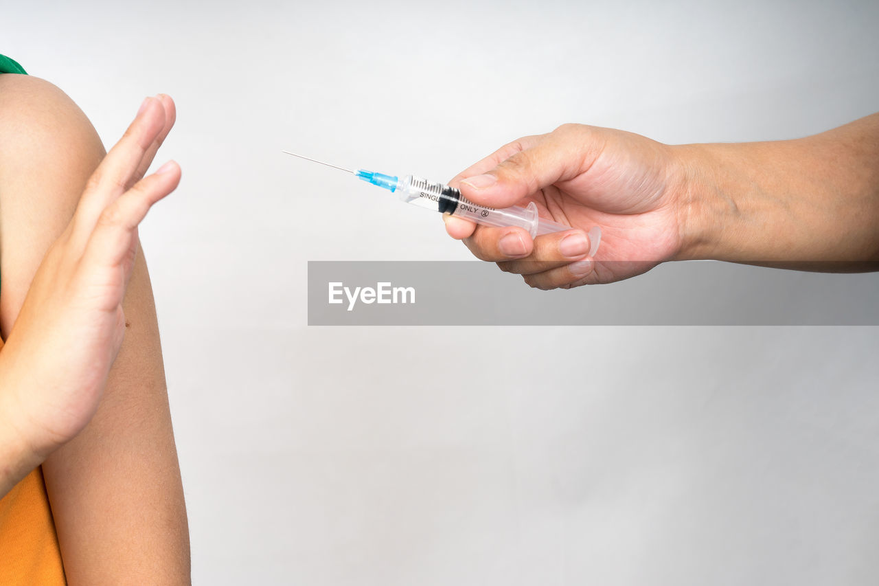 Cropped hand of doctor holding syringe while patent gesturing against gray background