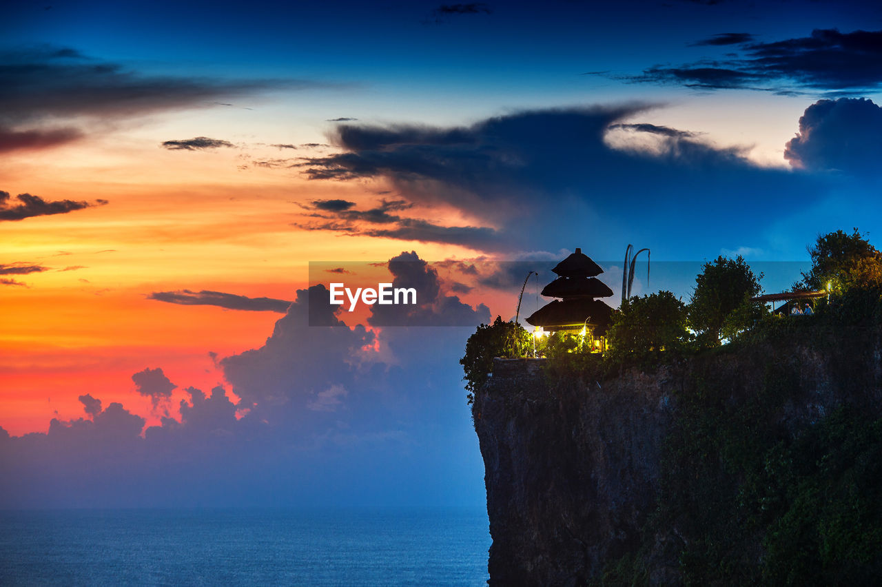 Uluwatu temple on cliff by sea against sky during sunset