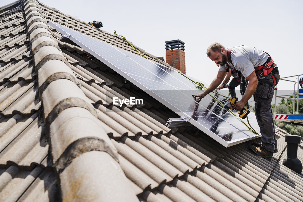 Electricians installing solar panels on rooftop of house