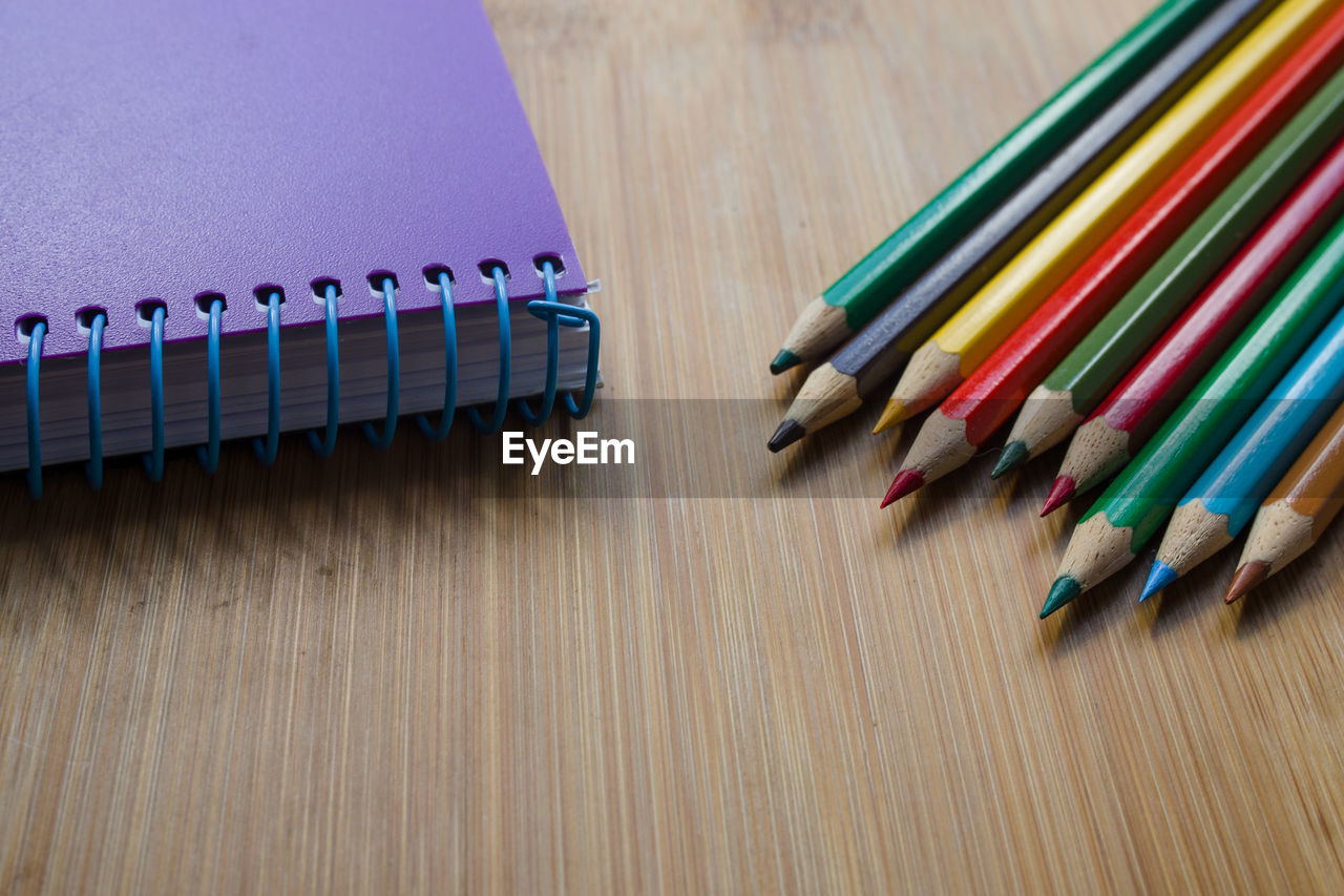 Colorful pencils with book on wooden table