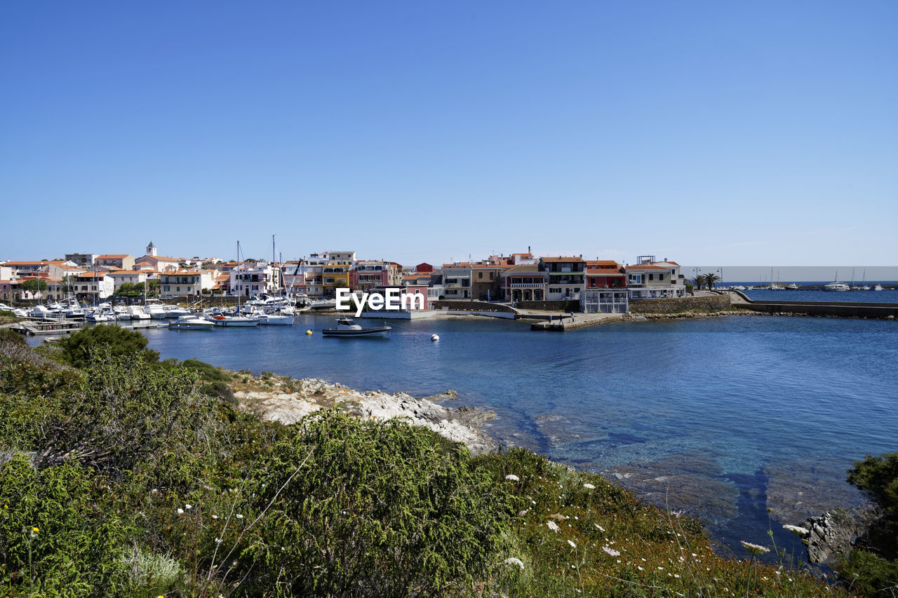 Sailboats in city by sea against clear sky