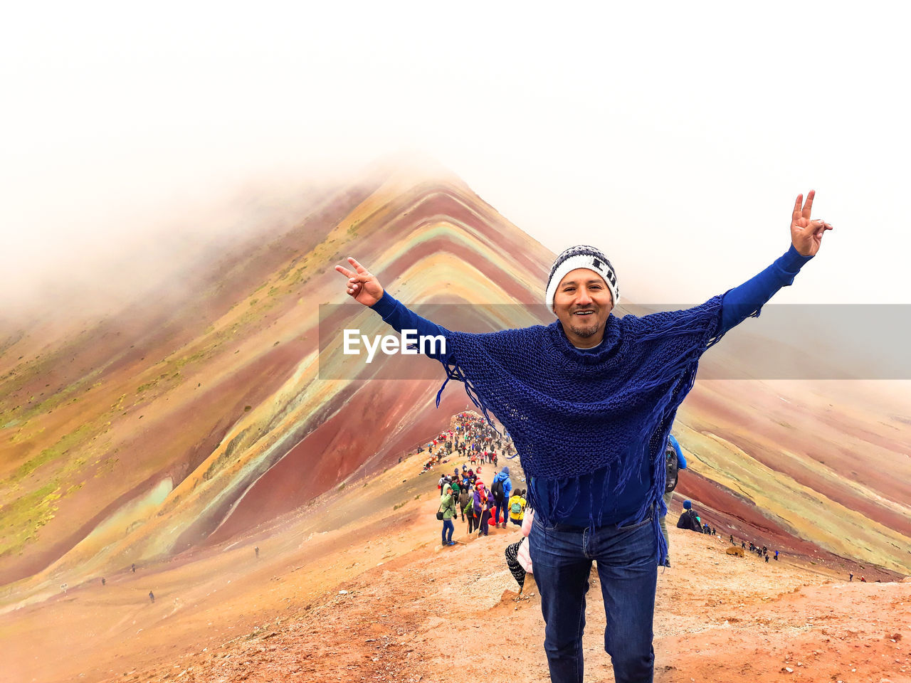 Portrait of man with arms outstretched standing against mountain during foggy weather