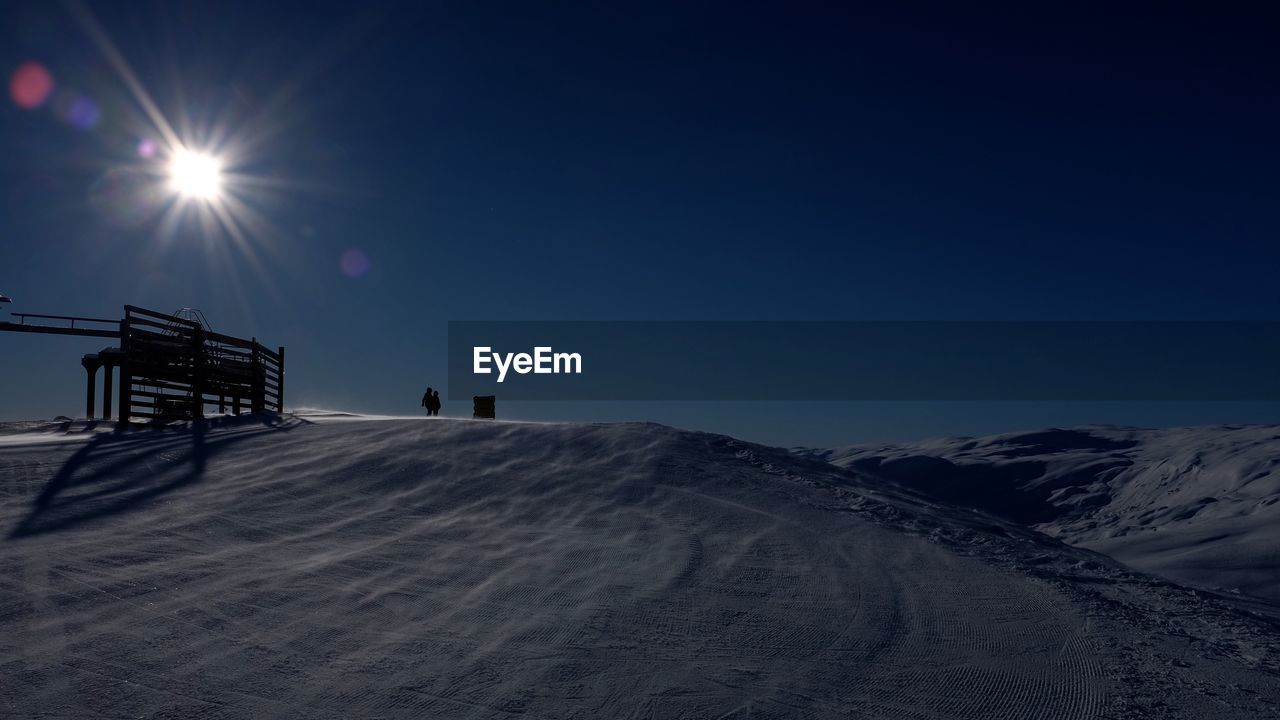 Low angle view of snow covered hill against blue sky on sunny day