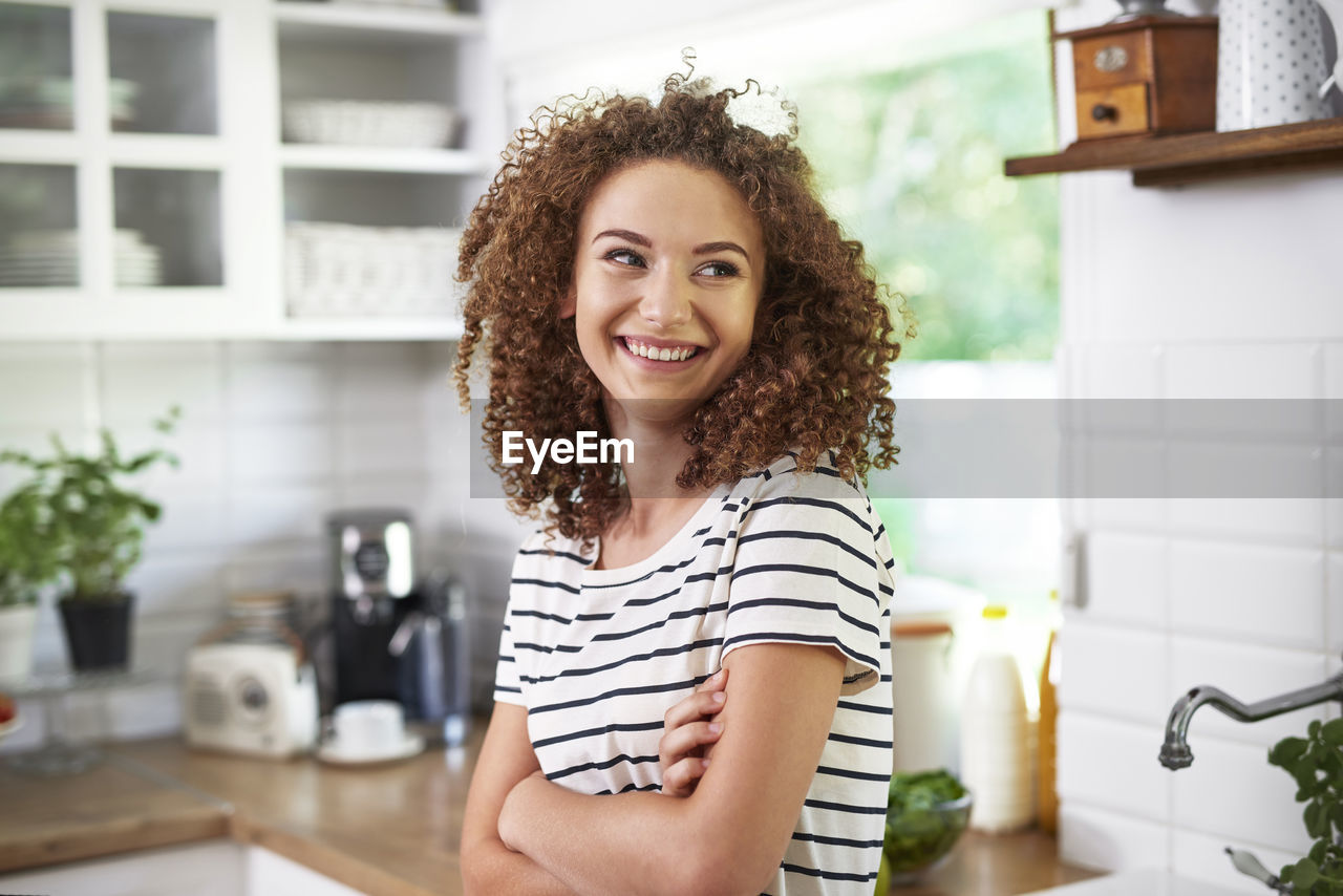 Smiling teenage girl with arms crossed standing in kitchen at home