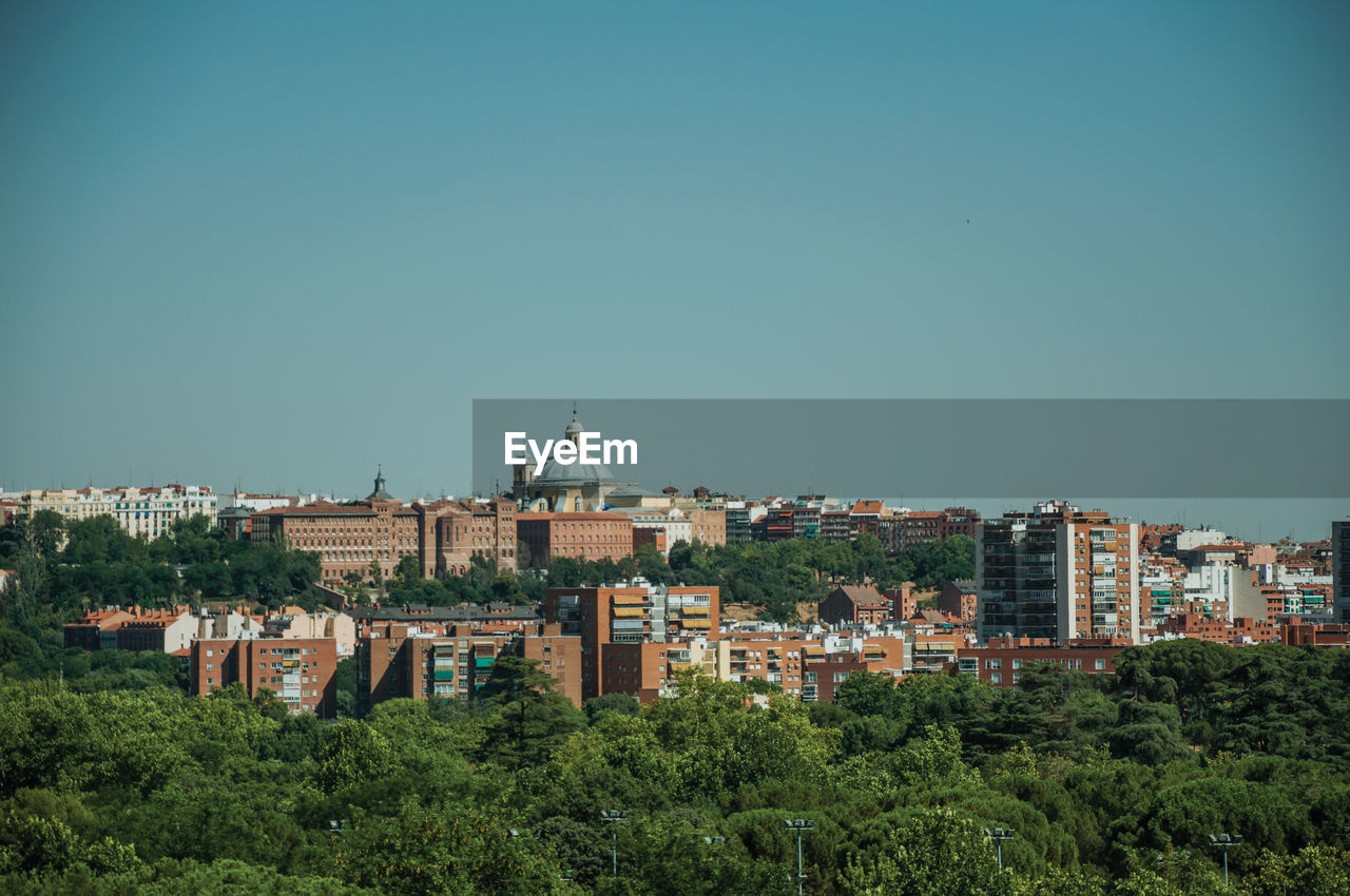 Building skyline on the horizon with green treetops seen from the teleferico park of madrid, spain.