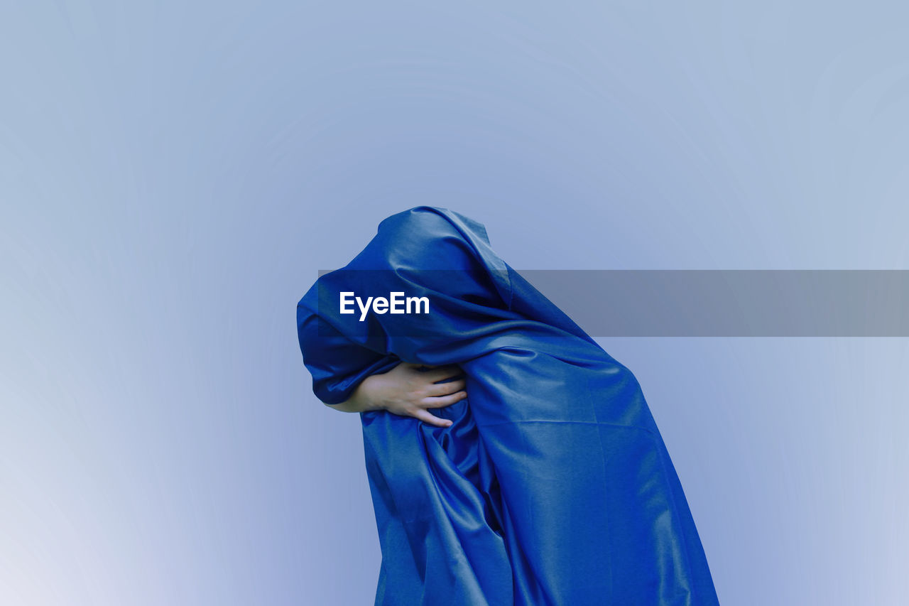 Girl covered with blue fabric against colored background
