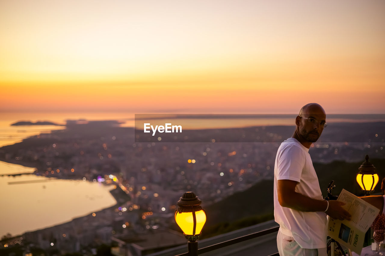 Rear view of man standing by sea against sky during sunset