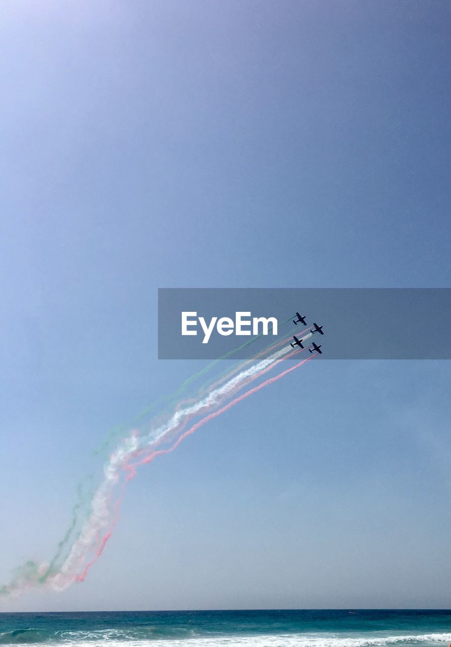 low angle view of airplane flying over sea against clear blue sky