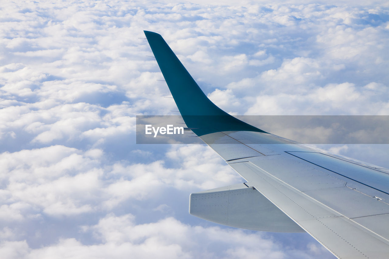 Cropped image of airplane wing flying over cloudy sky