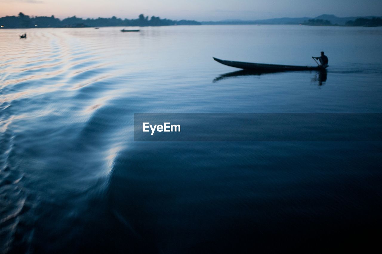 Silhouette man sailing on traditional boat on river against sky at dusk