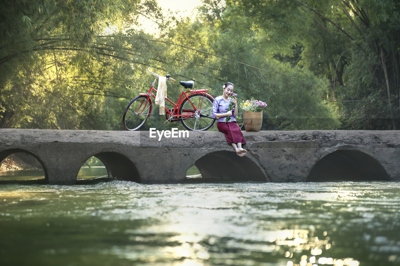 Woman sitting on arch bridge over river in forest