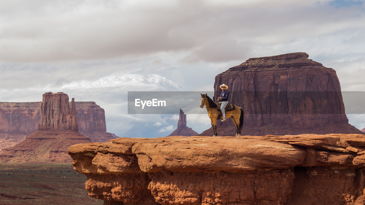 Full length of man sitting on horse over rocky cliff against sky