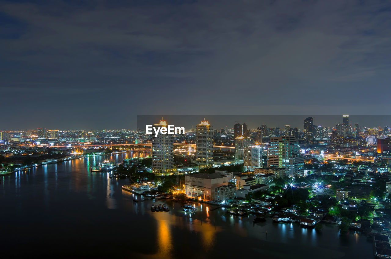 Illuminated buildings by river against sky in city at night