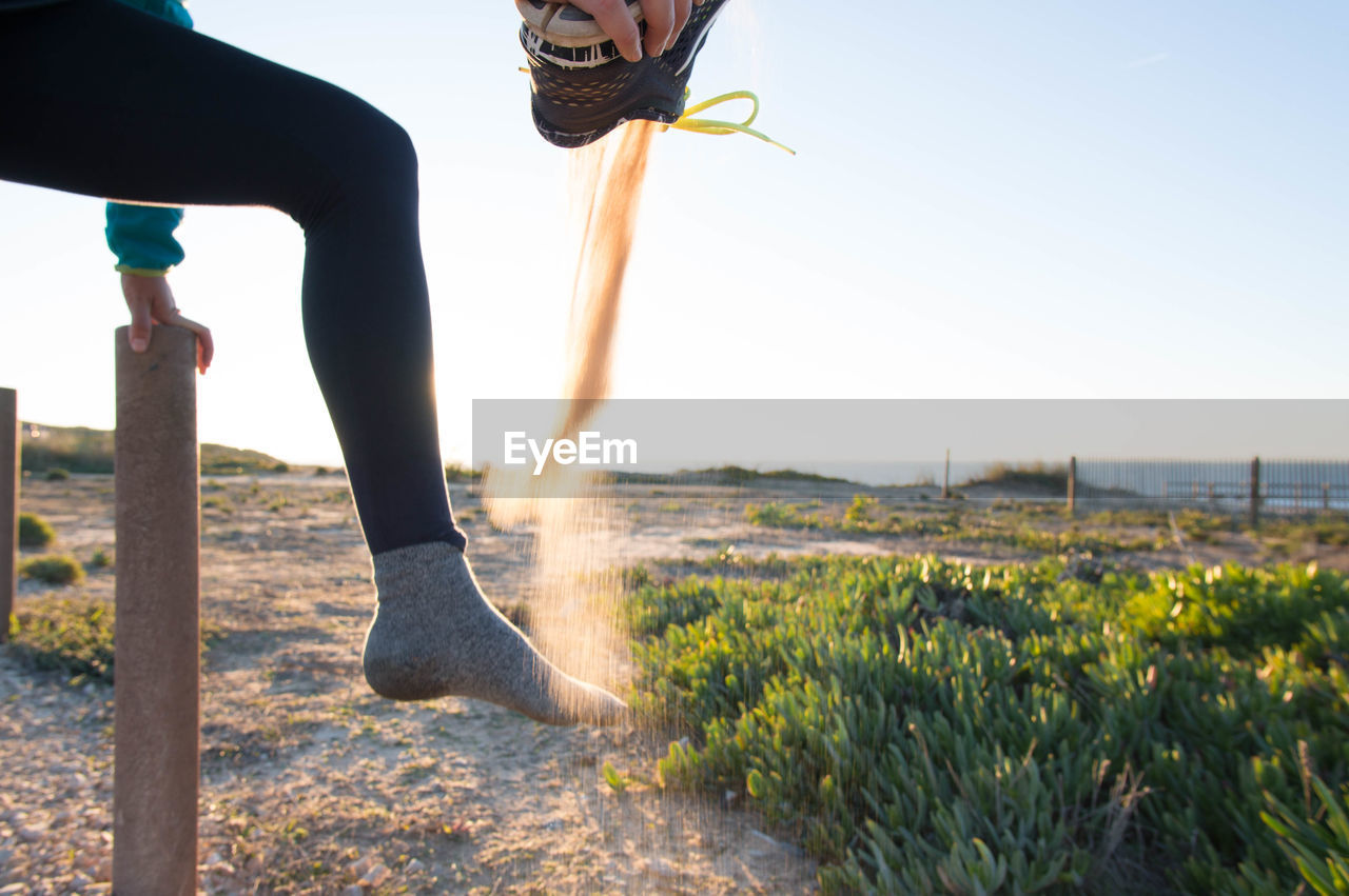 Low section of woman playing with sand at beach against clear sky