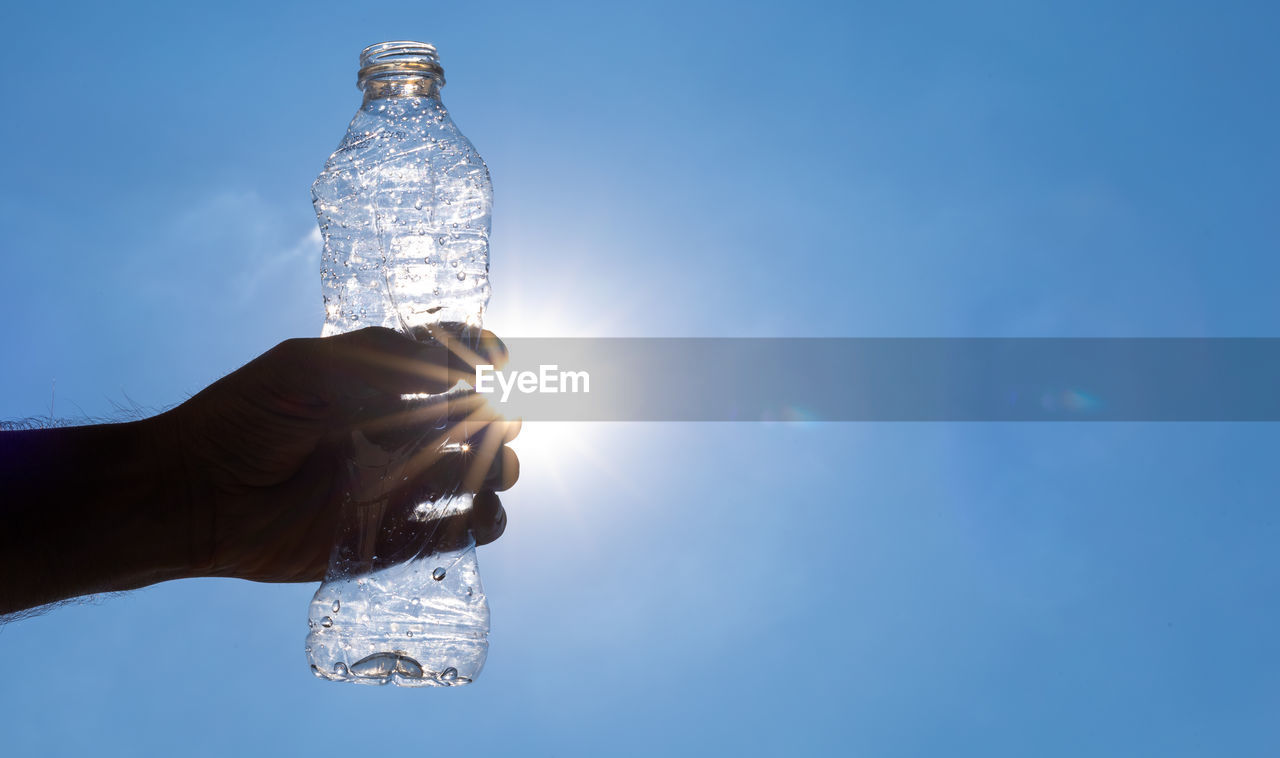 Hand holding glass bottle against blue sky