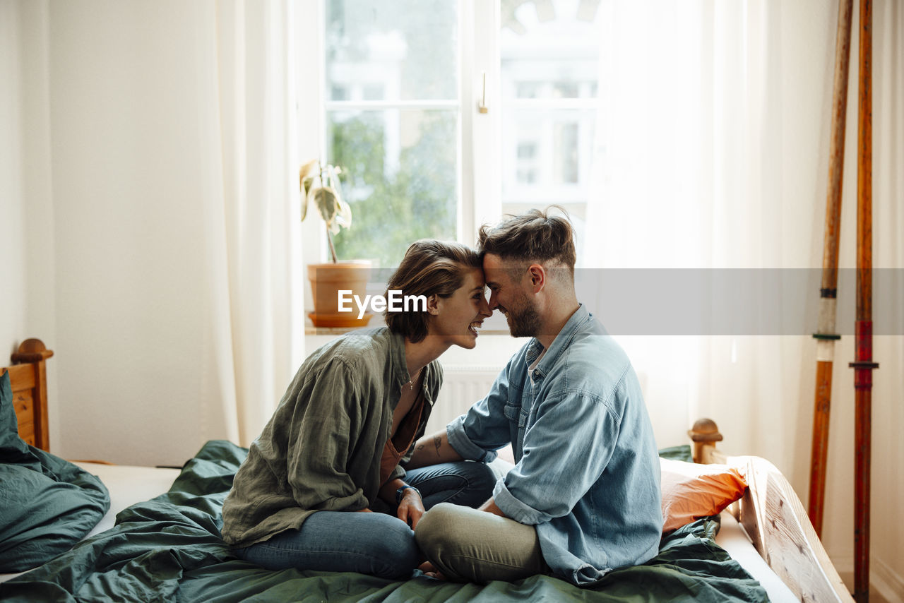 Couple touching foreheads while sitting on bed at home