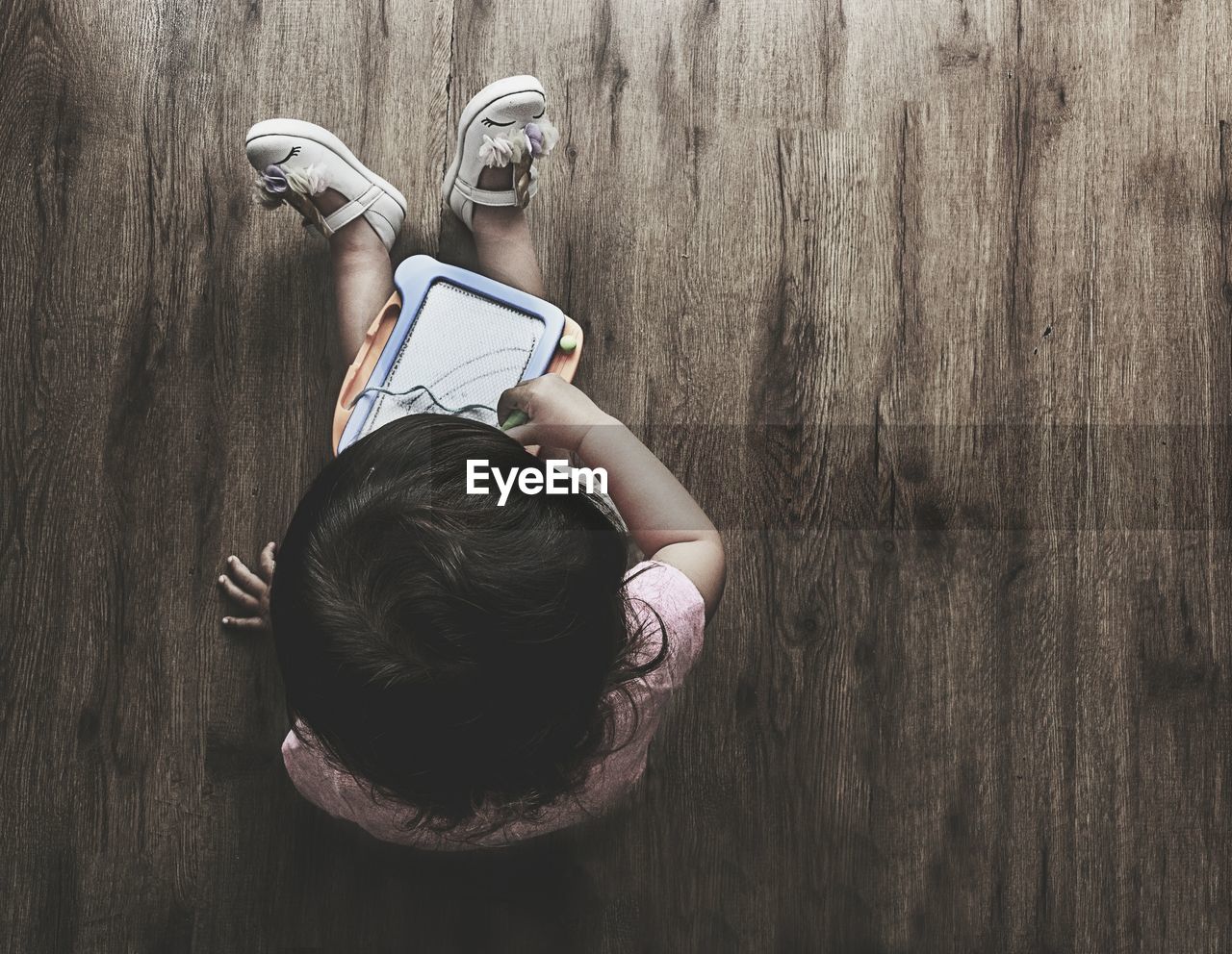 High angle view of girl with slate sitting on hardwood floor at home