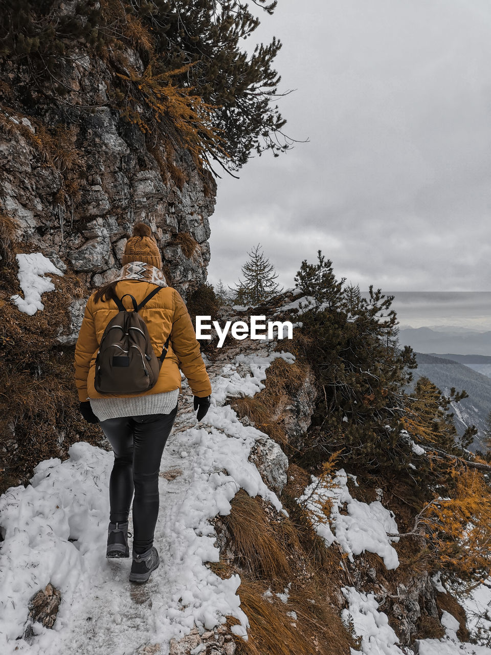 Rear view of young woman hiking on snowy path in mountains