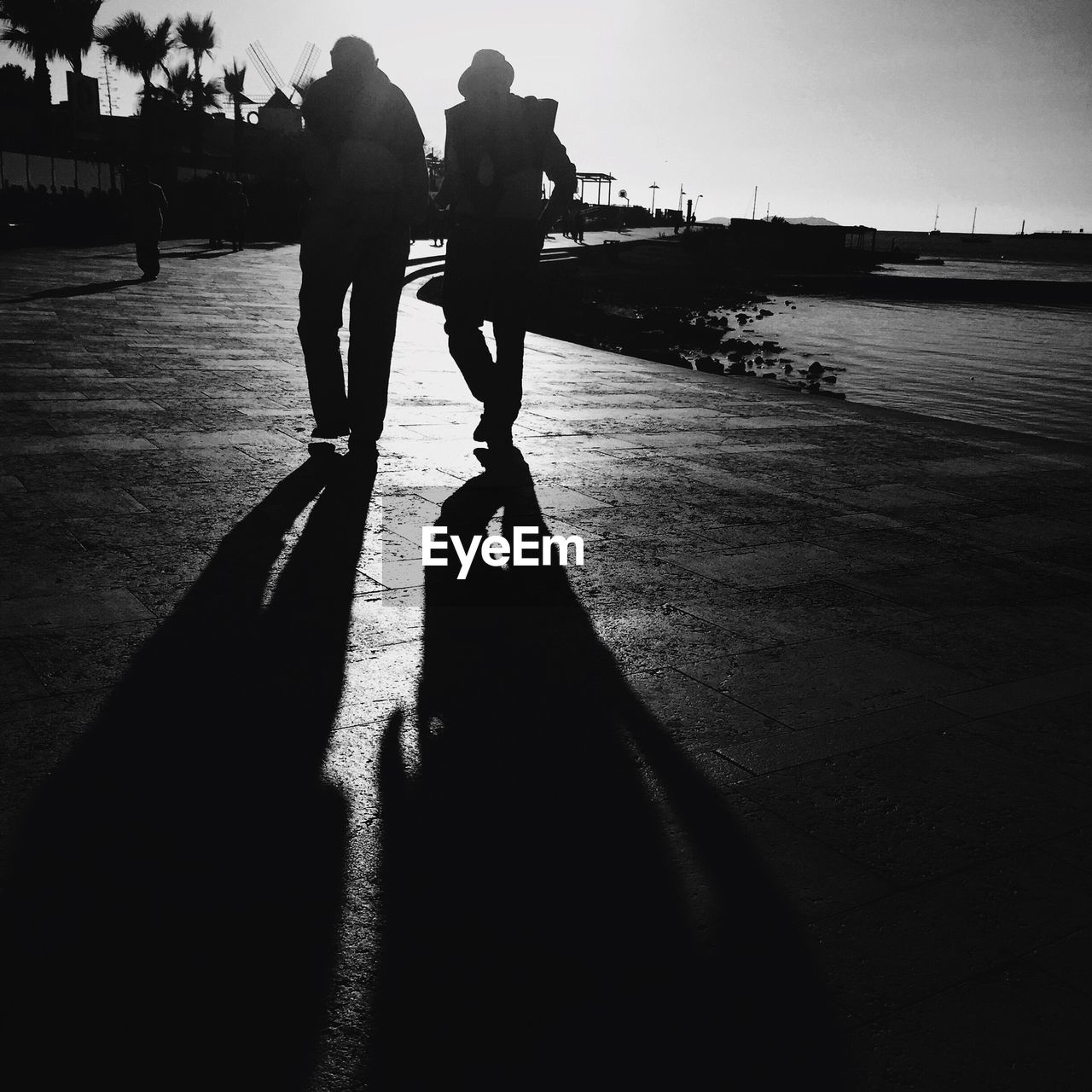 Silhouette men walking on sidewalk by sea against clear sky