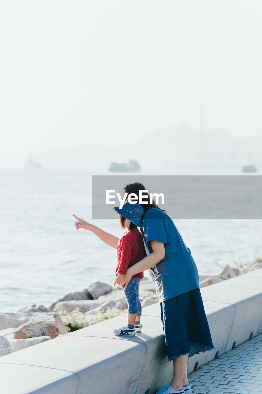 REAR VIEW OF COUPLE LOOKING AT SEA