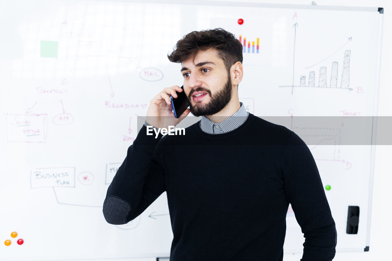 Businessman talking on phone in front of whiteboard in office