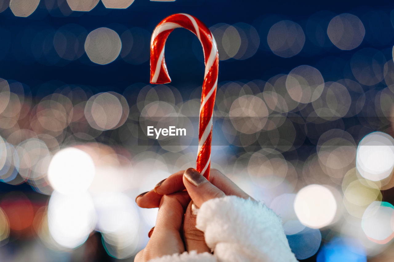 Christmas holiday magic details. female hands holding red white cane sweet lollipop