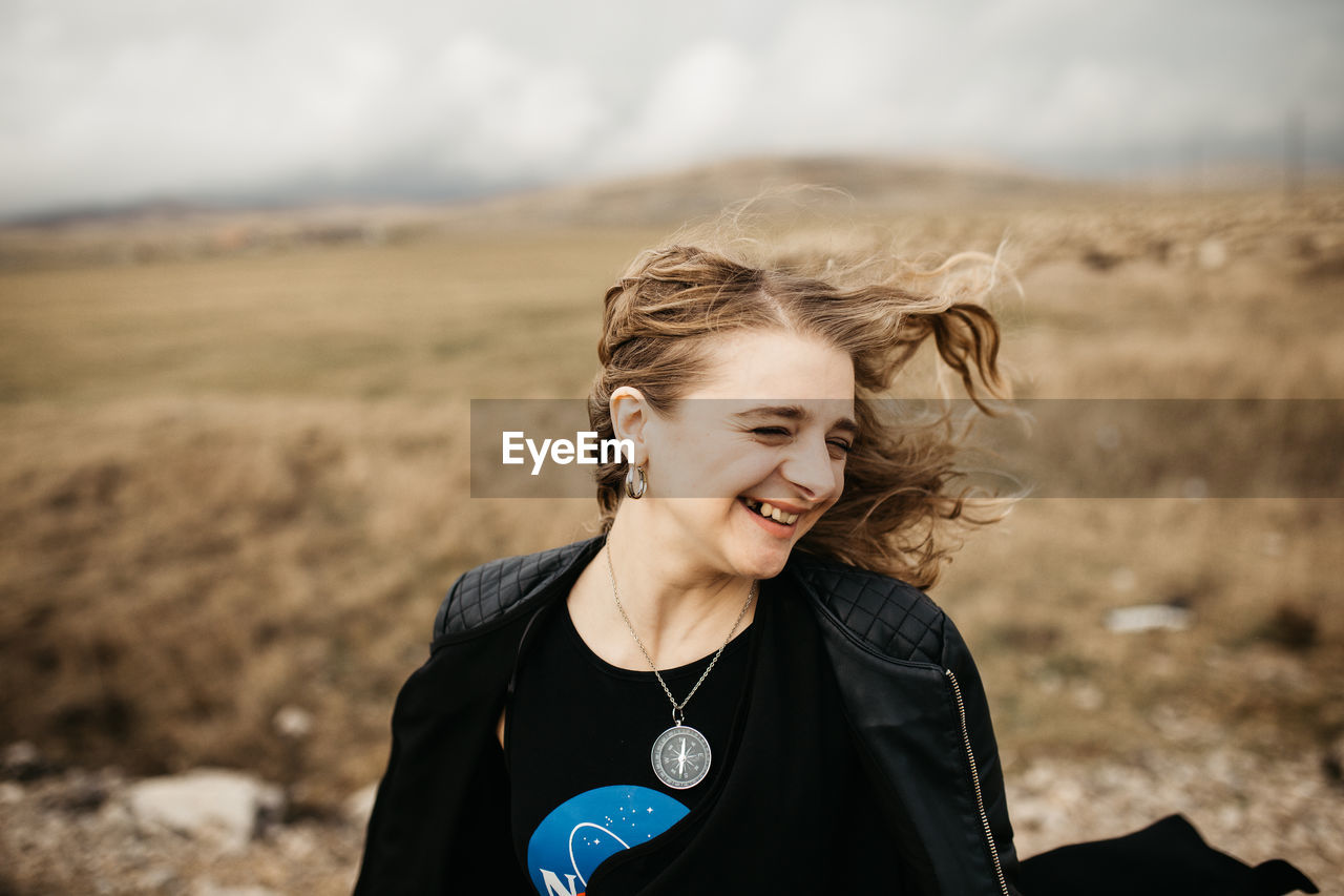 PORTRAIT OF SMILING YOUNG WOMAN ON FIELD