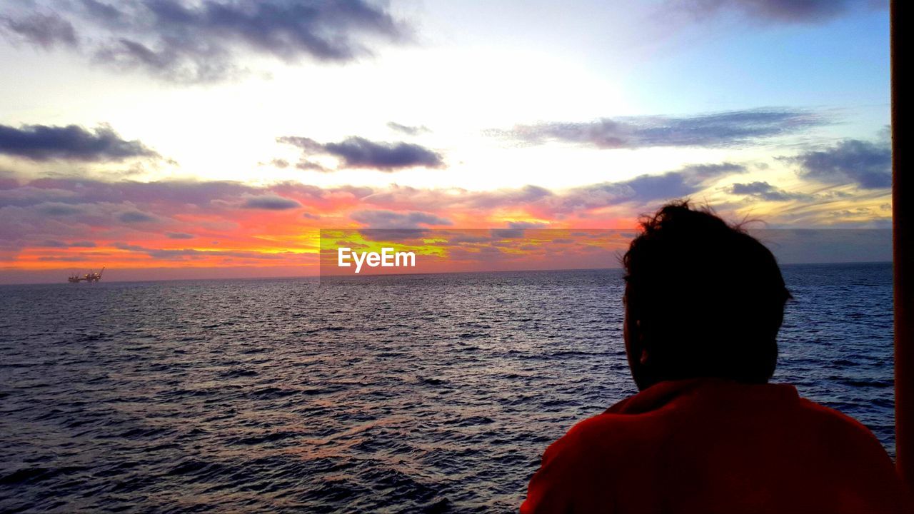 Rear view of man looking at sea during sunset