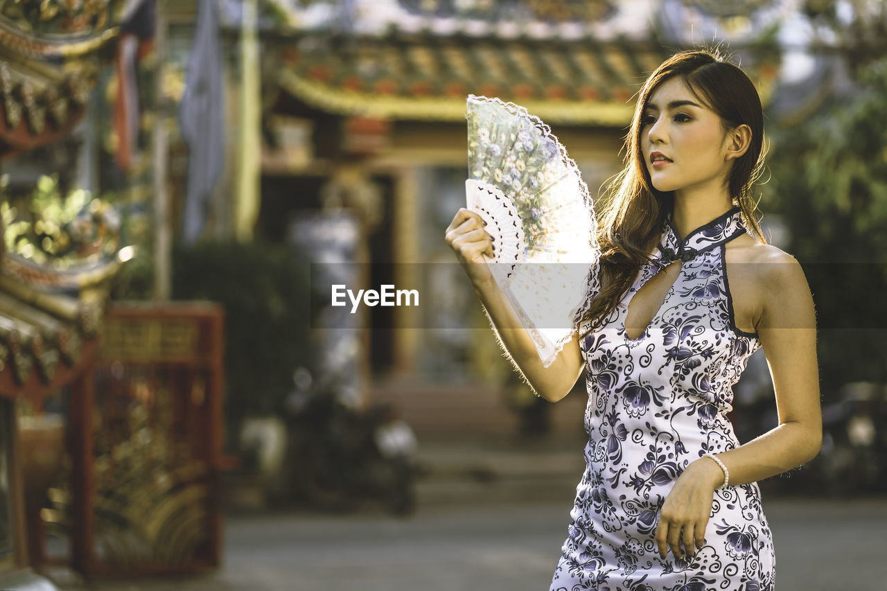 Young woman looking away while holding hand fan