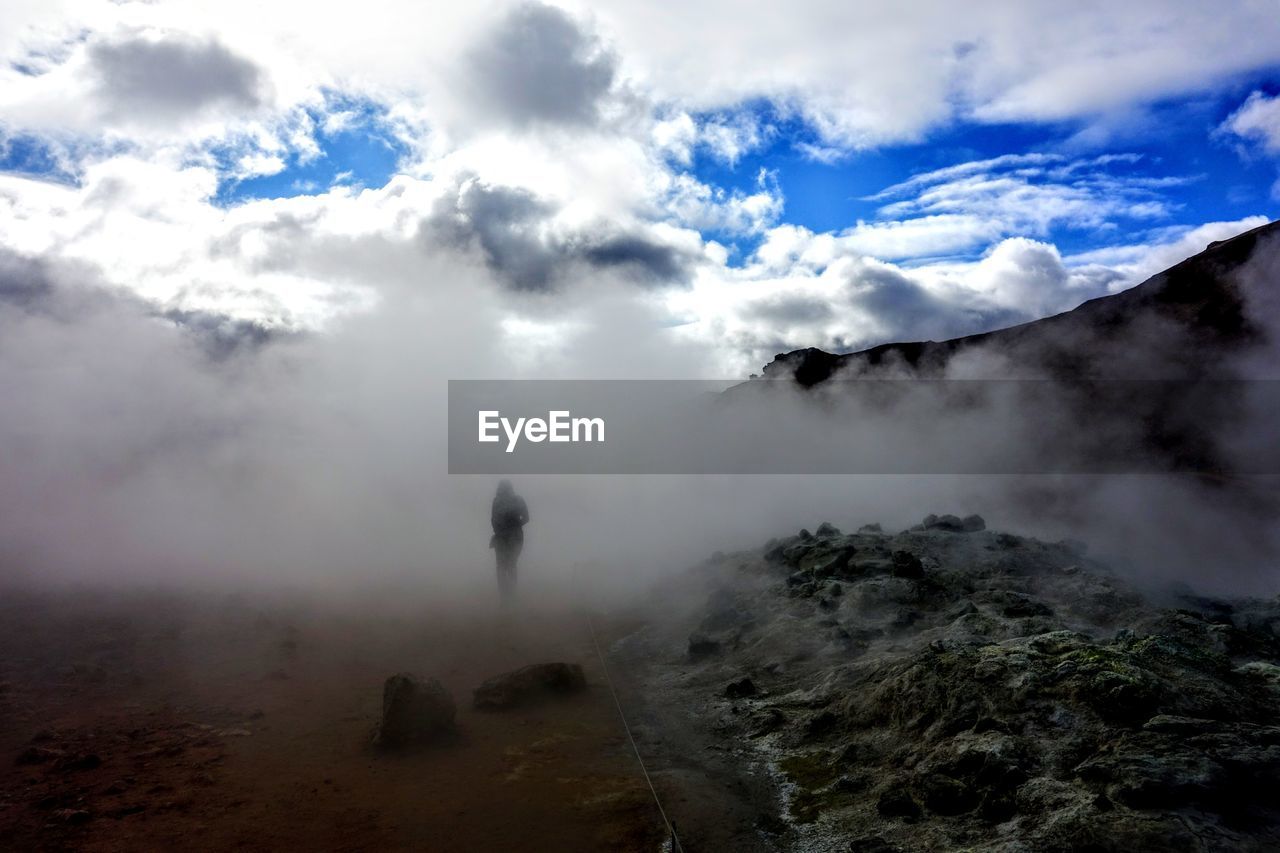 Woman standing amidst steam at hot spring against sky
