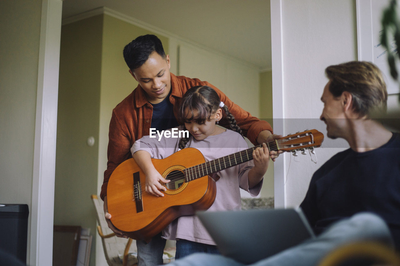 Gay father standing with daughter playing guitar at home
