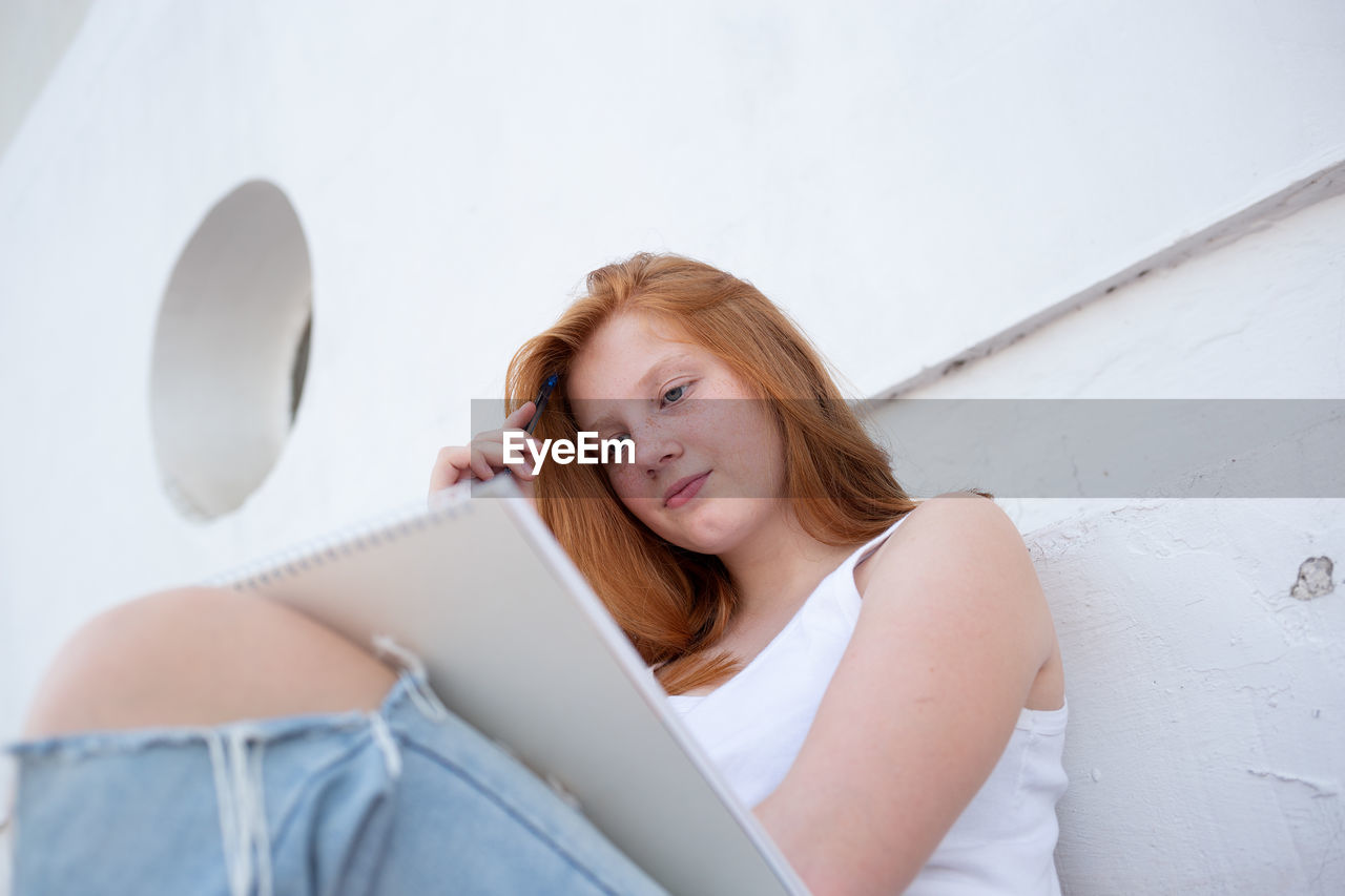 WOMAN USING PHONE WHILE SITTING ON WALL