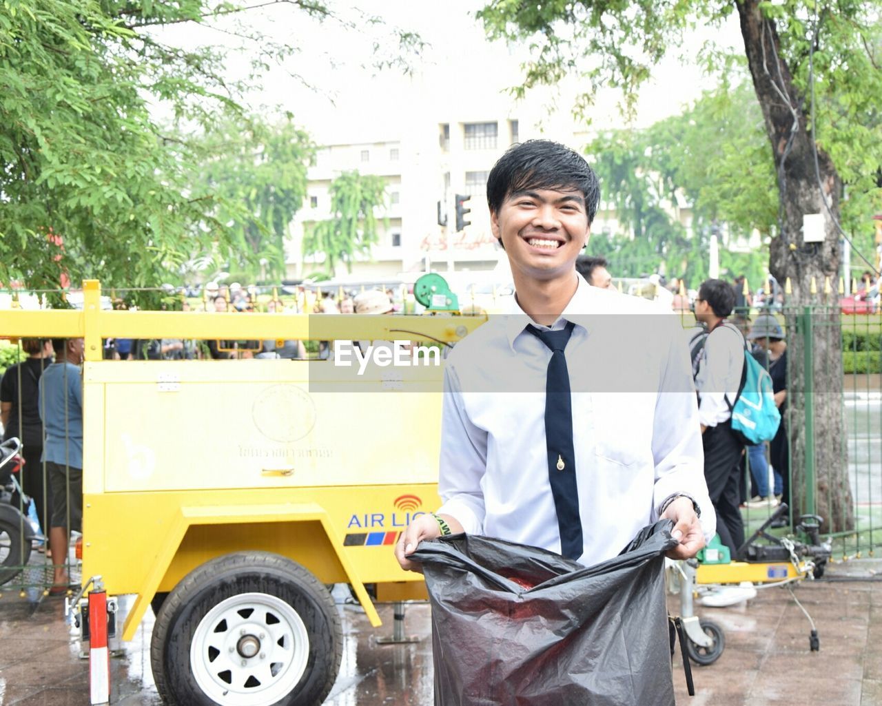 Portrait of smiling teenage boy holding garbage bag while standing by vehicle