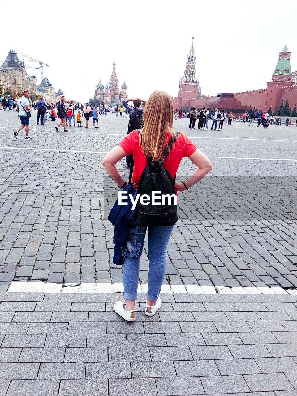 REAR VIEW OF WOMAN STANDING ON COBBLESTONE STREET