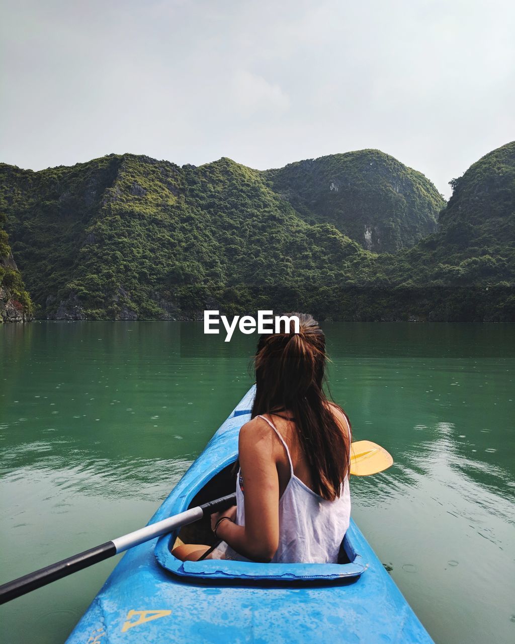 Rear view of woman kayaking on lake against mountains