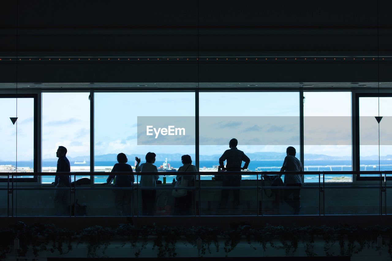 Silhouette people by railing against sky seen through glass window