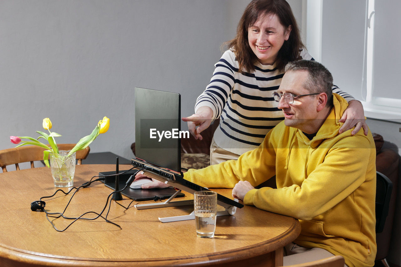 adult, technology, computer, men, two people, indoors, person, women, communication, sitting, smiling, wireless technology, table, furniture, female, emotion, togetherness, happiness, office, business, desk, laptop, casual clothing, occupation, working, internet, conversation, cooperation, child, mature adult, clothing, using laptop, positive emotion, lifestyles, eyeglasses, computer network, teamwork, using computer, home interior, yellow, computer equipment, glasses
