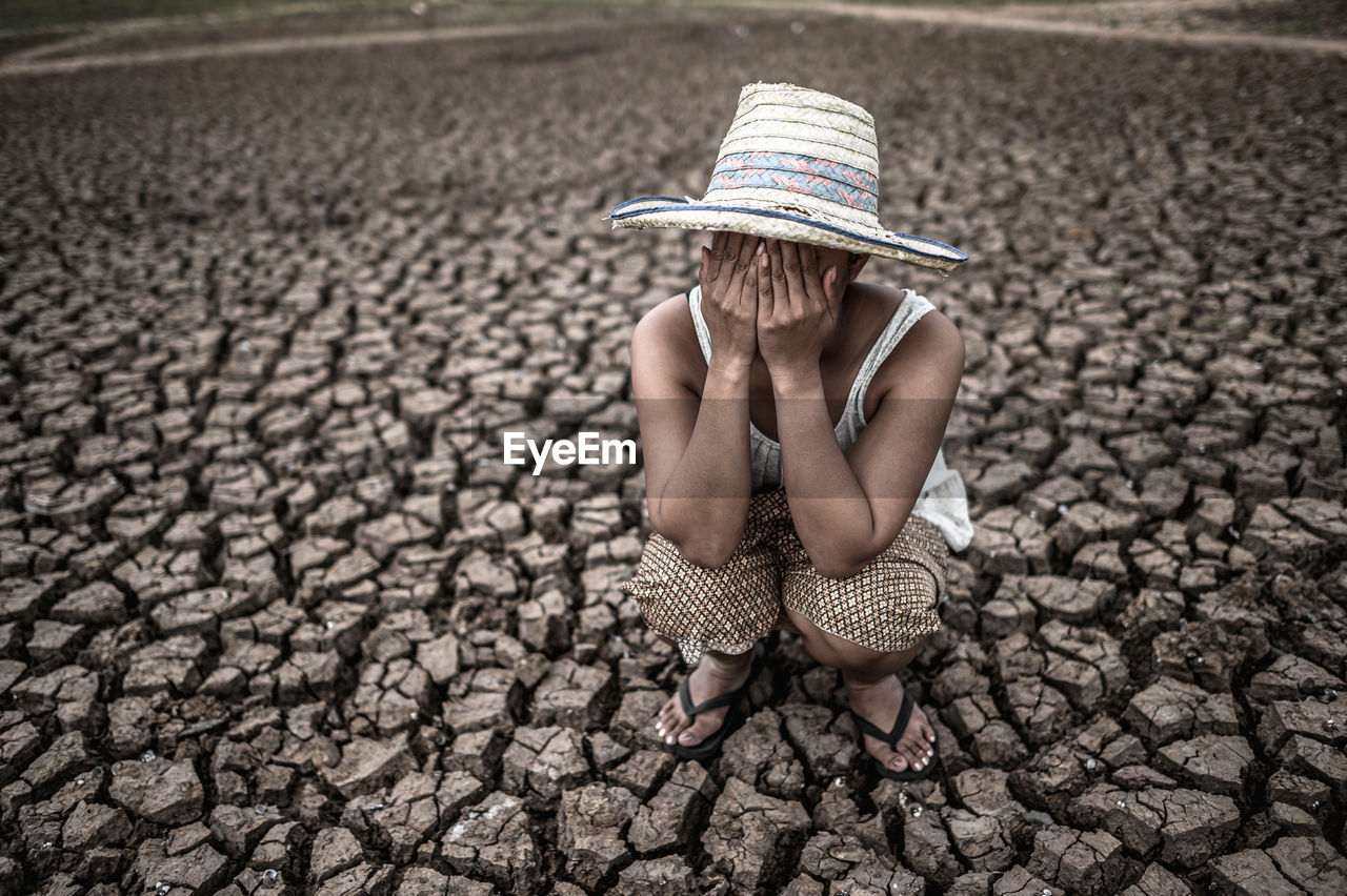 High angle view of woman wearing hat crying while crouching on land